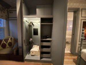 Grey painted hotel closet with shelves, drawers and an ironing board