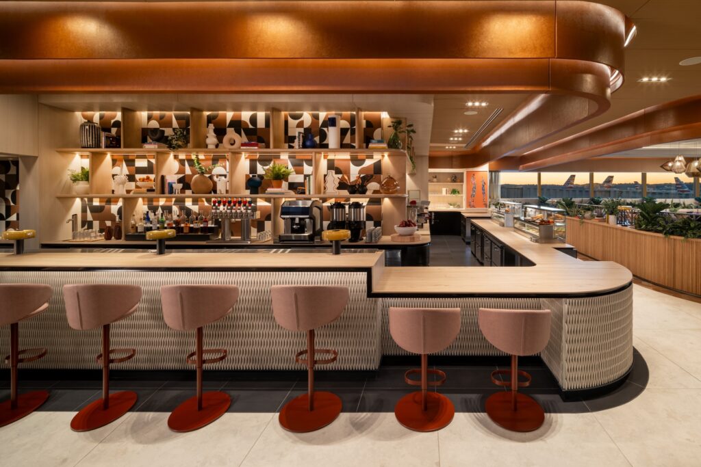 Five pink bar stools lined up against an ambient-lit bar at Capital One's new lounge in DCA